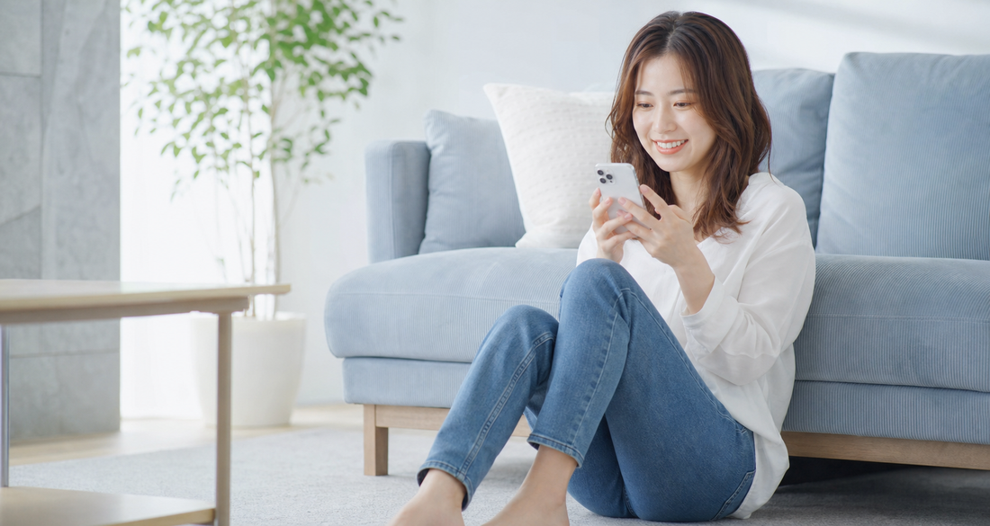 リビングでスマートフォンを見ながら微笑む女性